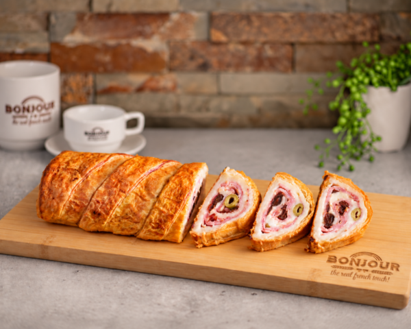 Pan de jamón de hojaldre de Bonjour Bakery, elaborado con masa de hojaldre dorada y relleno tradicional de jamón, aceitunas y pasas, presentado en rebanadas.